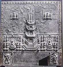 Relief with a pagoda in the centre surrounded by various images of deities. The lower part of the plaque bears an inscription which is framed by two deities.