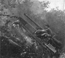 A tracked vehicle fitted with a large gun negotiates its way up a steep hillside (of about forty-five degrees, or one-in-one). The crew of two in the open cab are leaning forward and holding on tightly to avoid falling out backwards.