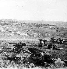 A battery of four artillery guns deployed in the field surrounded by treeless hills