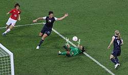 Soccer game between Japan and United States. Goalkeeper Hope Solo lies on the ground saving a ball, while Wambach is next to her.