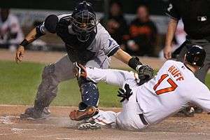 A baseball player tries to slide in to home plate while a catcher puts down a tag