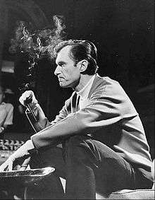 Black-and-white photo of a seated Hugh Hefner, smoking his trademark pipe