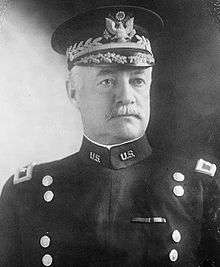 Man facing forward in dress uniform with two vertical columns of buttons and hat with gold trim