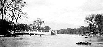 A destroyed bridge with a part with one end attached to the shore and the other end in the water; the other part is missing.