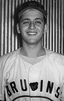 A man smiles for the camera in a baseball cap and jersey with "Bruins" written across the chest.