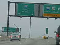 A split in a freeway with two green signs over the road. The left sign reads Interstate 95 Trenton Chester with two downward arrows and the right sign reads east Interstate 676 east U.S. Route 30 Ben Franklin Bridge upper right arrow exit only.
