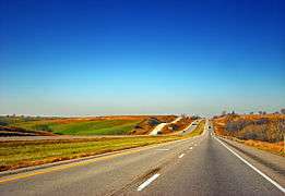 A highway underneath a clear sky surrounded by harvested cropland and green pastures