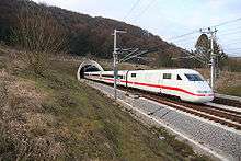 White electric train with red cheatline emerging from tunnel in the countryside