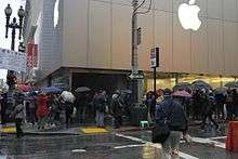 Customers standing in line in front of an Apple Store. The line is very long.