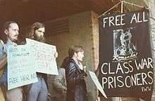 People holding signs near a banner demanding, "Free all class war prisoners!"