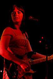 Colour photograph of Isa Maria performing live in 2007. She is playing underneath a red light, making her appear red.