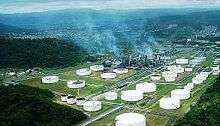 Aerial photo of oil refinery: many white storage tanks and smoke amid greenery