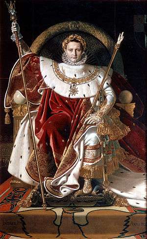 Man on throne wearing elaborate red, white, and gold gowns made of velvet and fur.
