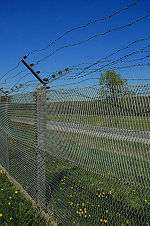 Expanded metal fence against a blue sky with rows of barbed wire lining the top