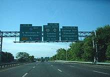 A multilane freeway surrounded by trees with three green signs over the road. The left sign reads exit 2 Interstate 76 west Walt Whitman Bridge Philadelphia toll upper left arrow E-ZPass, the middle sign reads exit 1A north U.S. Route 130 south Route 168 Camden Trenton 1/2 mile, and the right sign reads exits 1C-B Collings Avenue Gloucester Collingswood 1/4 mile.