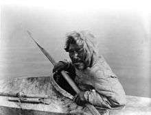 Photograph of an Inuit man seated in a kayak, holding a paddle