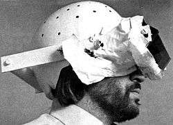 A set of mirrors attached via a harness and a helmet to a man's head; the mirrors show the man his own body reflected upside down, and a covering blocks his view of anything other than the mirror.