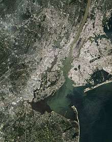 A satellite image of New York City and the adjacent areas of New Jersey. Most water is dark green, but the Hudson River is light brown, and that continues into the bay south of it.