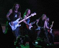 A color photograph of members of the band Iron Maiden on stage with guitars