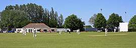 Cricket being played in front of the pavilion at Ironmould Lane
