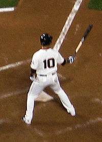 A baseball player with a black number 10 on the back of his uniform prepares to hit