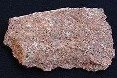 A rough chunk of granite showing grains of red, pink, white, gray and black.