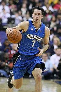A fair-skinned man is dribbles a basketball. He is wearing a blue basketball uniform with the word "ORLANDO" on the jersey.