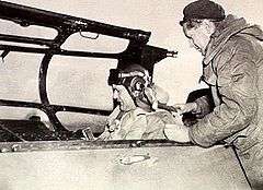 Man in flying helmet putting on a harness in the cockpit of a military aircraft