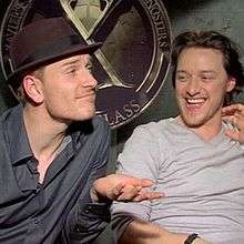 Michael Fassbender and James McAvoy sit in front of the "X" logo for Xavier's school.