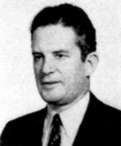 Grainy older portrait of a caucasian man wearing a suit and a tie. He is facing left, and has dark curly hair.