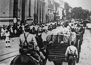 A black-and-white photo showing Japanese troops, some on horsebacks, entering Saigon.