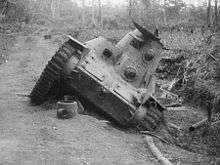 A small tank on a road, which is at a 45 degree angle due to one side being in the ditch beside the road.