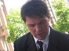 Jágr, a caucasian man with short, brown hair, has his head turned down slightly and is wearing a black suit and tie with a white dress shirt.