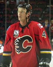 Hockey player in red uniform, with a large "C" in the middle. He looks to his right.