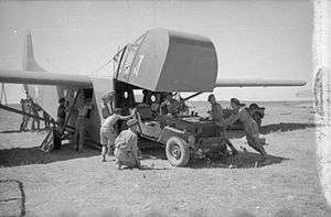 Waco glider with the front cockpit raised and four men pushing a jeep inside