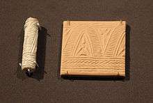 A carved cylindrical object and a small plaque of clay showing a repetitive geometric design