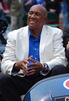 African-American man wearing a blue shirt and a white sportsjacket riding on a blue vehicle.