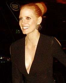 A woman with red hair in a top knot wearing a black dress with a plunging neckline.
