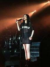 A picture of a woman standing in front of microphone wearing an oversized tee