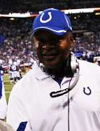 Color photograph of Jim Caldwell wearing a blue Indianapolis Colts hat and white sport shirt, headset around his neck, standing on football field sideline.
