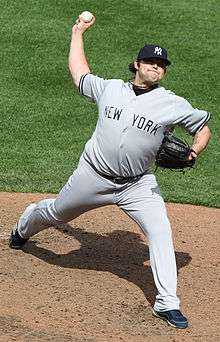 A man in a grey uniform with "NEW YORK" written in navy letters prepares to throw a ball.