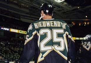 Backside of a hockey player, looking up. He is in a black and green uniform with the name "NIEUWENDYK" above a large number 25 on the back.