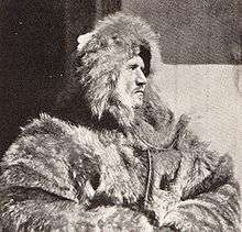 Head and upper body of a man, facing right. He is dressed in heavy fur clothing including a hat which conceals much of his face, although the profile is clear