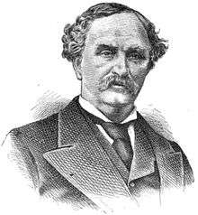 A man with dark, curly hair and a mustache wearing a dark jacket, vest, and tie and a white shirt