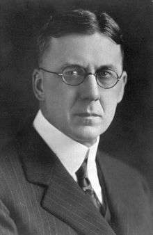 A severe-looking man wearing round-rimmed glasses
