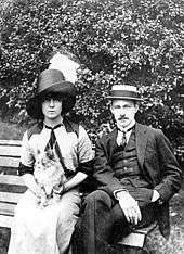 Barrymore and Katherine Corri Harris sitting on a park bench, both wearing jaunty hats and looking at the camera