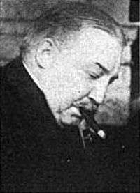 A black-and-white photograph of a balding man with his head bowed smoking a cigar, from the side