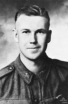 Head and shoulders of a man with short, dark hair. His tunic is buttoned at the collar and he wears Australian Army "rising sun" badges.