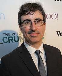 Headshot of comedian John Oliver, wearing a suit and glasses
