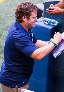 Candid waist-up photograph of Schneider wearing a blue shirt and signing an autograph.